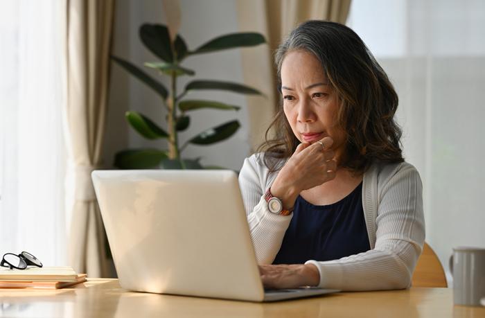 Older Asian woman looking at laptop with contemplative pose Older Asian woman looking at laptop with contemplative pose